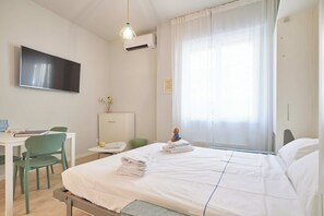 Ein Hotelzimmer mit einem Bett, einem Schreibtisch mit Stuhl, einem Fernseher und einem Fenster mit Vorhängen.