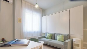 Ett modernt vardagsrum med en soffa, ett bord med en bok, en väggmonterad luftkonditioneringsanläggning och en hängande lampa.