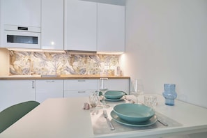 Eine moderne Küche mit weißen Schränken, einer gemusterten Spritzschutzwand und einem Essbereich mit Tisch für zwei Personen.