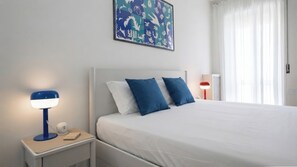A hotel room with a bed, a nightstand with a lamp, and a painting on the wall. - Italianway Comfort - Torre 24 (Milano)