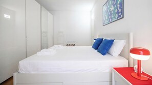 Ein Hotelzimmer mit Bett, weißer Bettwäsche, einer roten Nachttischlampe und einem Wandbild.
