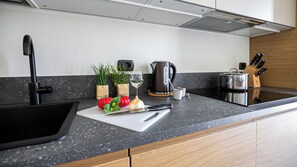 A modern kitchen with a black sink, a white cutting board with vegetables, a kettle, and a knife block. - Italianway Comfort - Torre 24 (Milano)