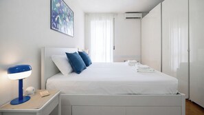 A neatly made bed with pillows, a bedside table with a lamp, and a folded towel on the floor. - Italianway Comfort - Torre 24 (Milano)
