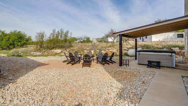 An outdoor seating area with Adirondack chairs and a grill, surrounded by a gravel patio and a covered structure. - Gorgeous Lake View in Sportsman’s World (Strawn)