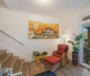 Una escalera conduce a una sala de estar con una silla de mimbre, un cuadro y plantas en macetas.