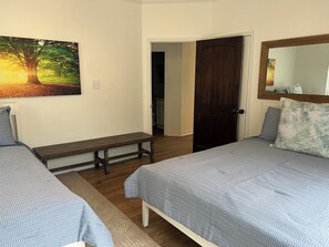 Un dormitorio con dos camas, un banco, una puerta y un cuadro en la pared.