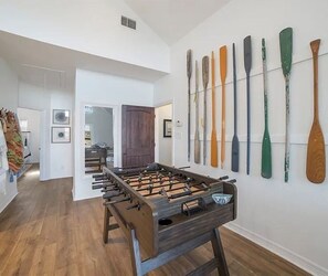 A room with a foosball table, wooden flooring, and a wall displaying various paddles.