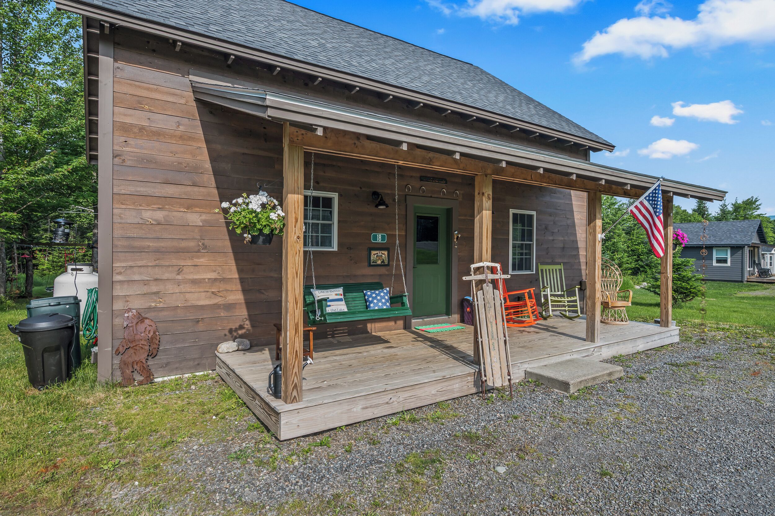 A wooden cabin with a porch, a green door, and a bench.