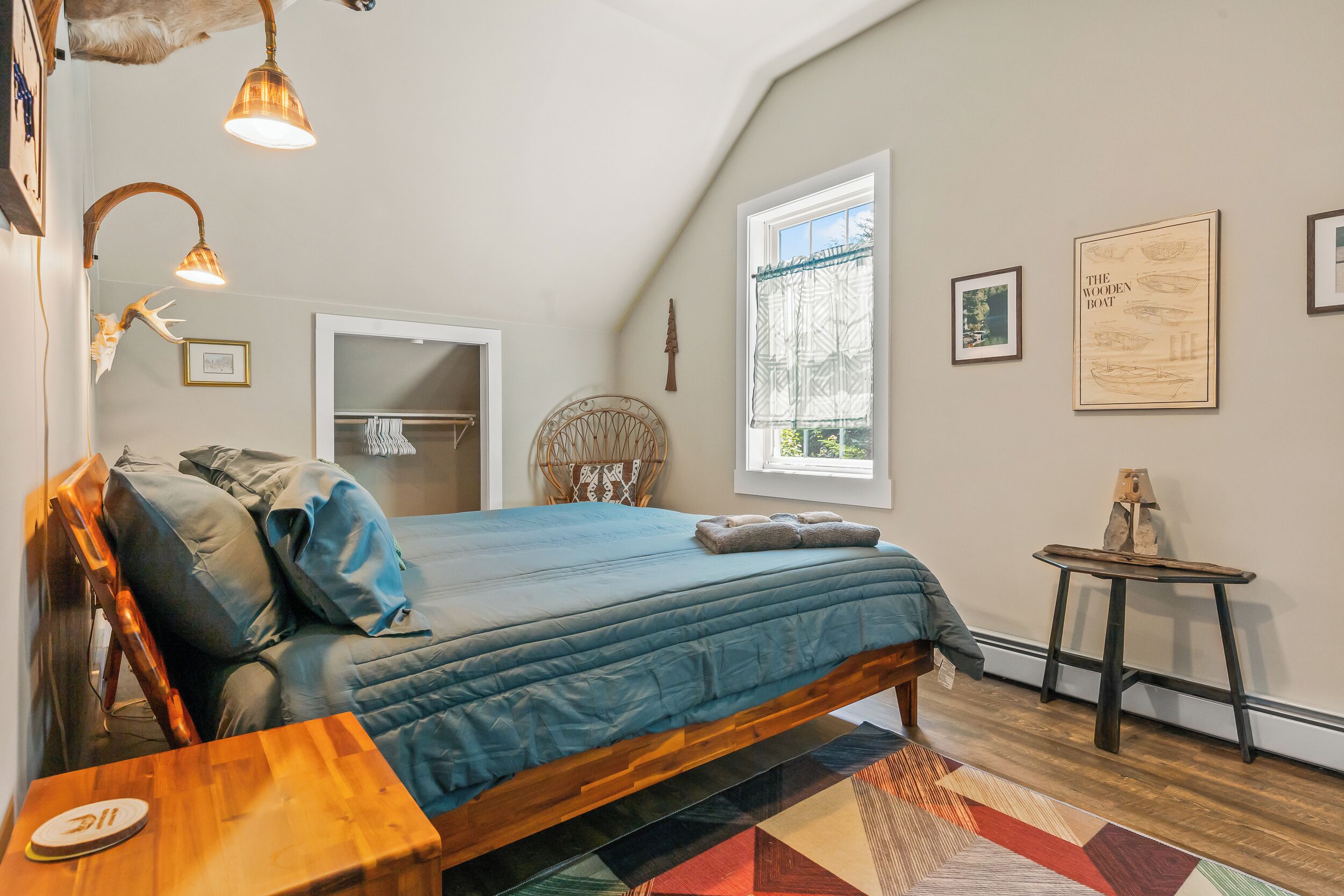 A bedroom with a bed, a wooden nightstand, a small table, a window, and wall art.