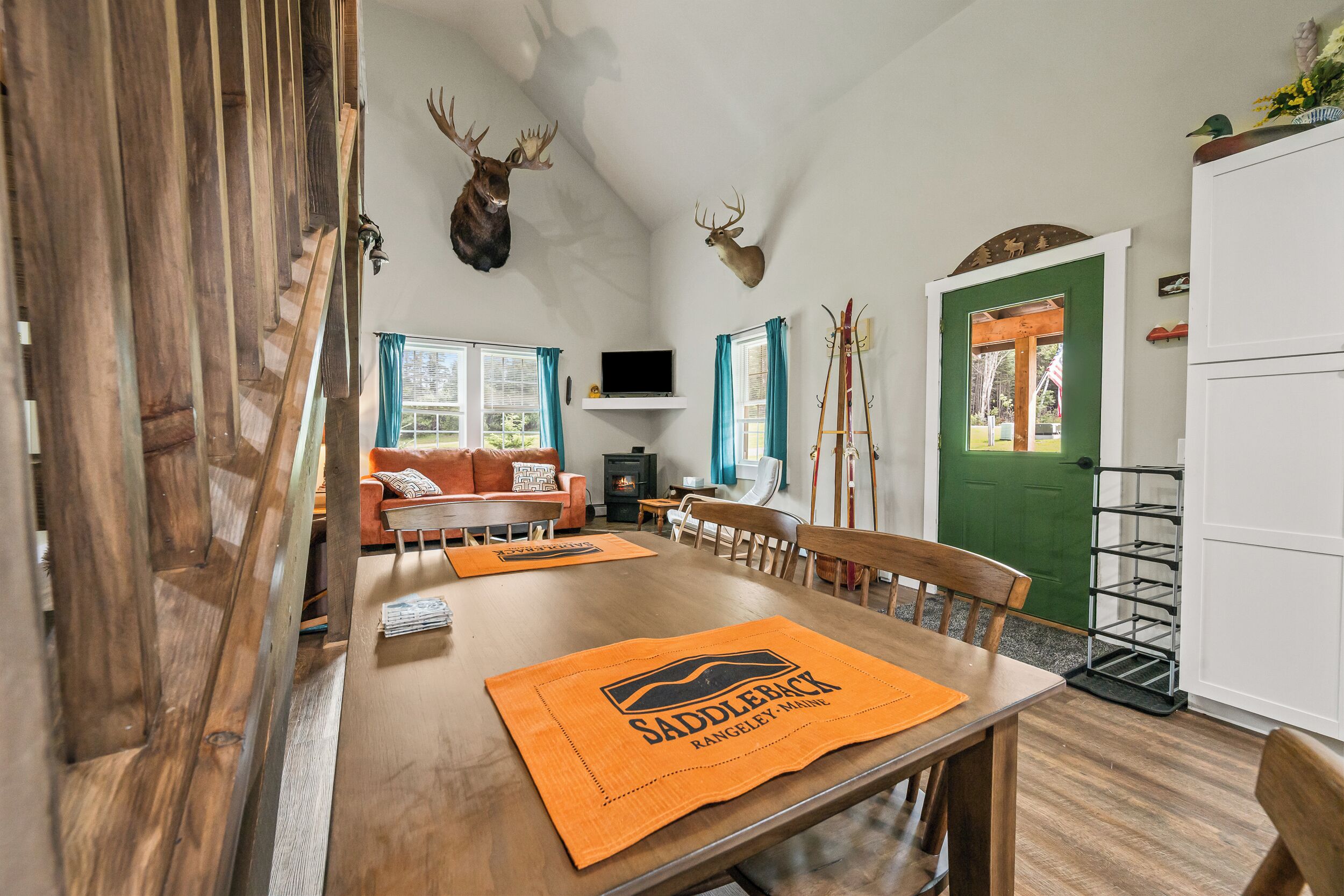 Ein Essbereich mit einem Holztisch, Stühlen und orangefarbenen Platzsets mit der Aufschrift 'Saddleback Rangeley, Maine'.