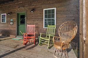 A wooden cabin with a green door, two rocking chairs, and a wicker chair on the porch. - Hildy's Hideaway | NEW! Sleeps 10 | Direct Snowmobile Access | Near Saddleback & Downtown (Rangeley)