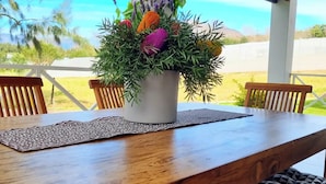 A wooden dining table with a potted plant centerpiece, surrounded by chairs with patterned cushions.
