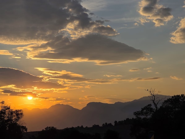 A sunset over a mountainous landscape with silhouettes of trees and a clear sky. - mon Reve Estate (Paarl)