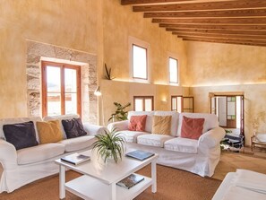 Ein geräumiges Wohnzimmer mit Steinwand, einer weißen Sofagarnitur und einem Couchtisch mit Büchern.