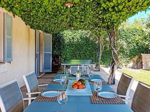 Ein Essbereich im Freien mit einem Tisch für vier Personen, umgeben von Pflanzen und einer Pergola.
