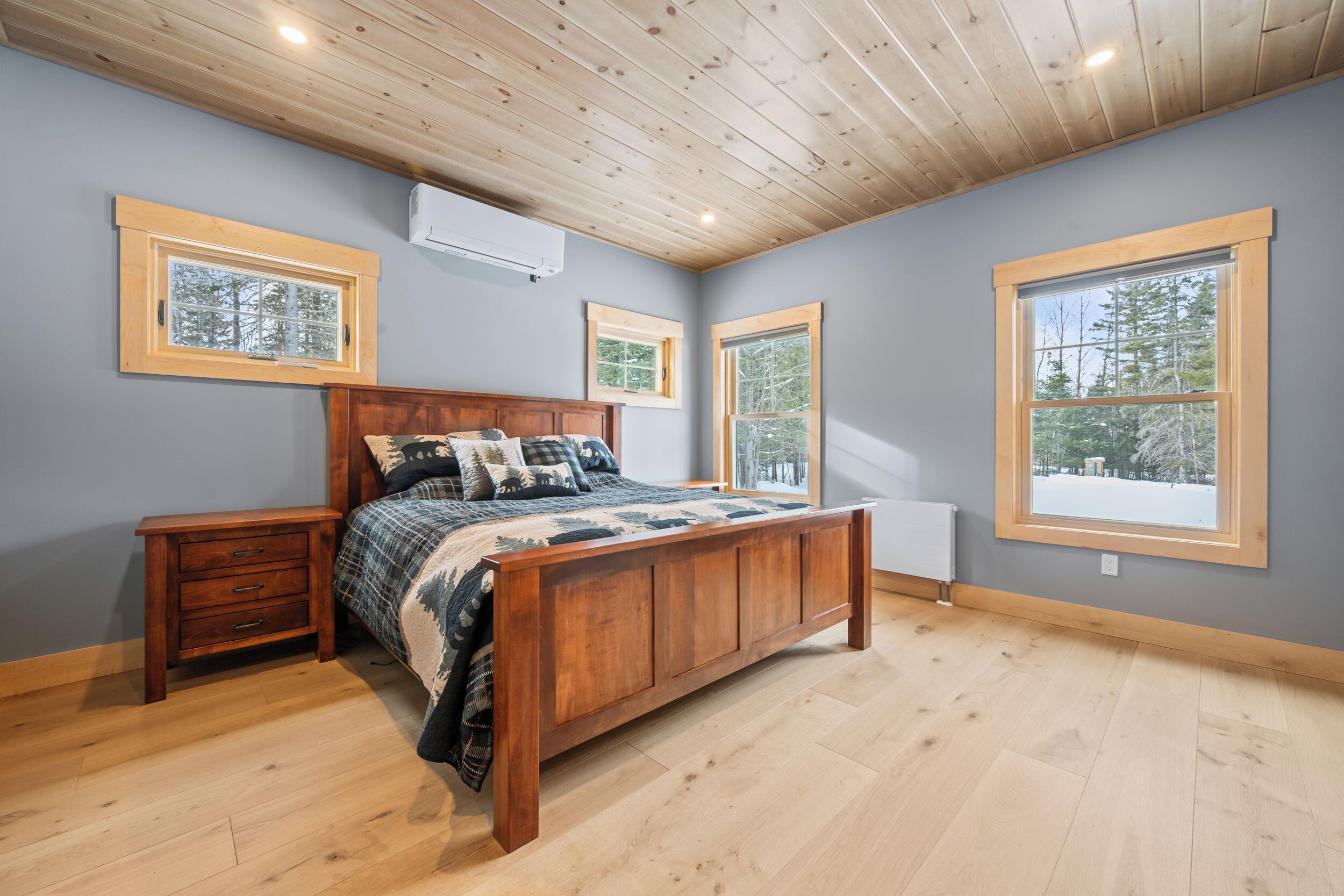 A bedroom with a wooden bed, nightstands, a radiator, and large windows with views of trees.