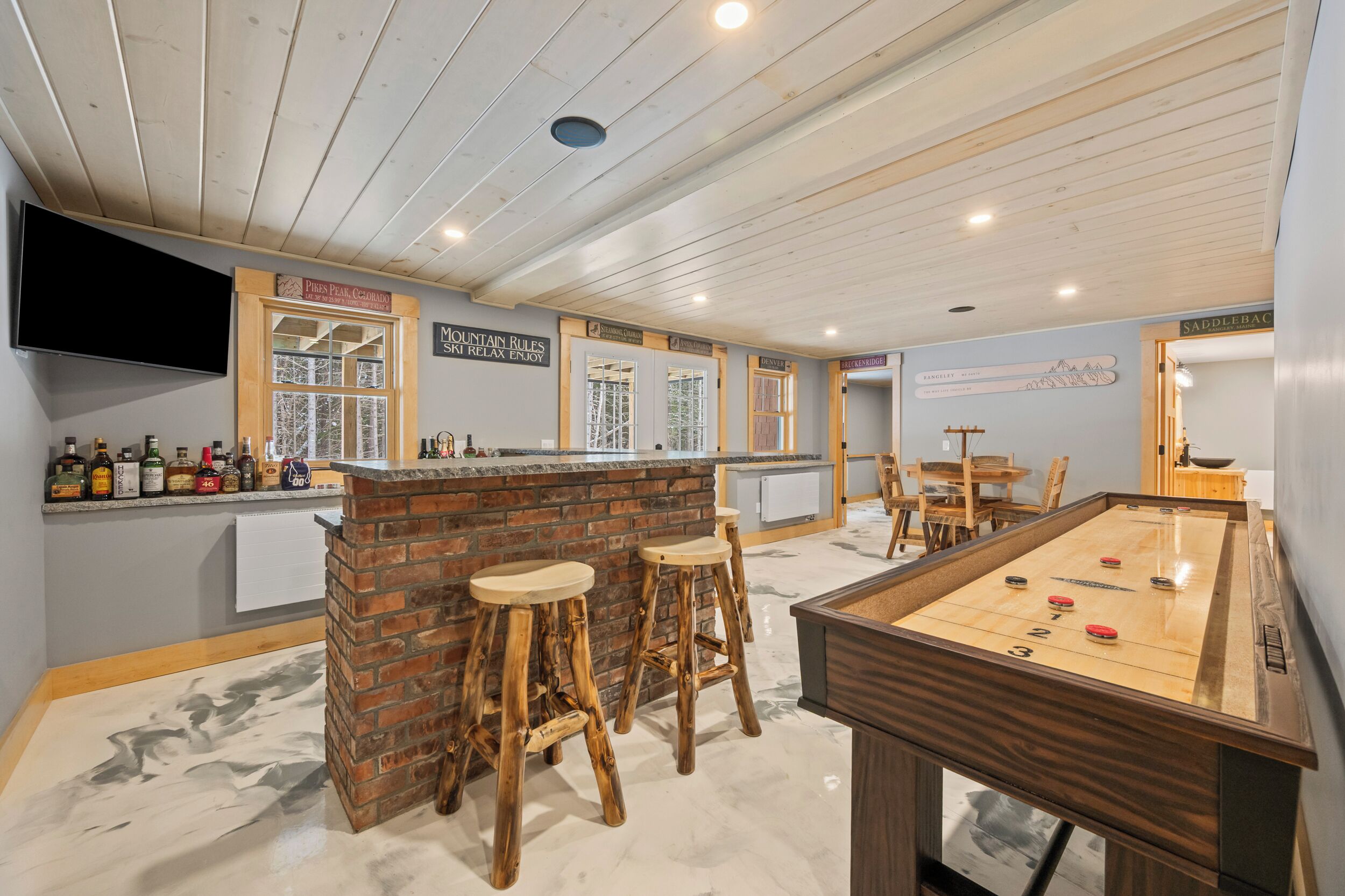 A bar area with a pool table, stools, and a television mounted on the wall.