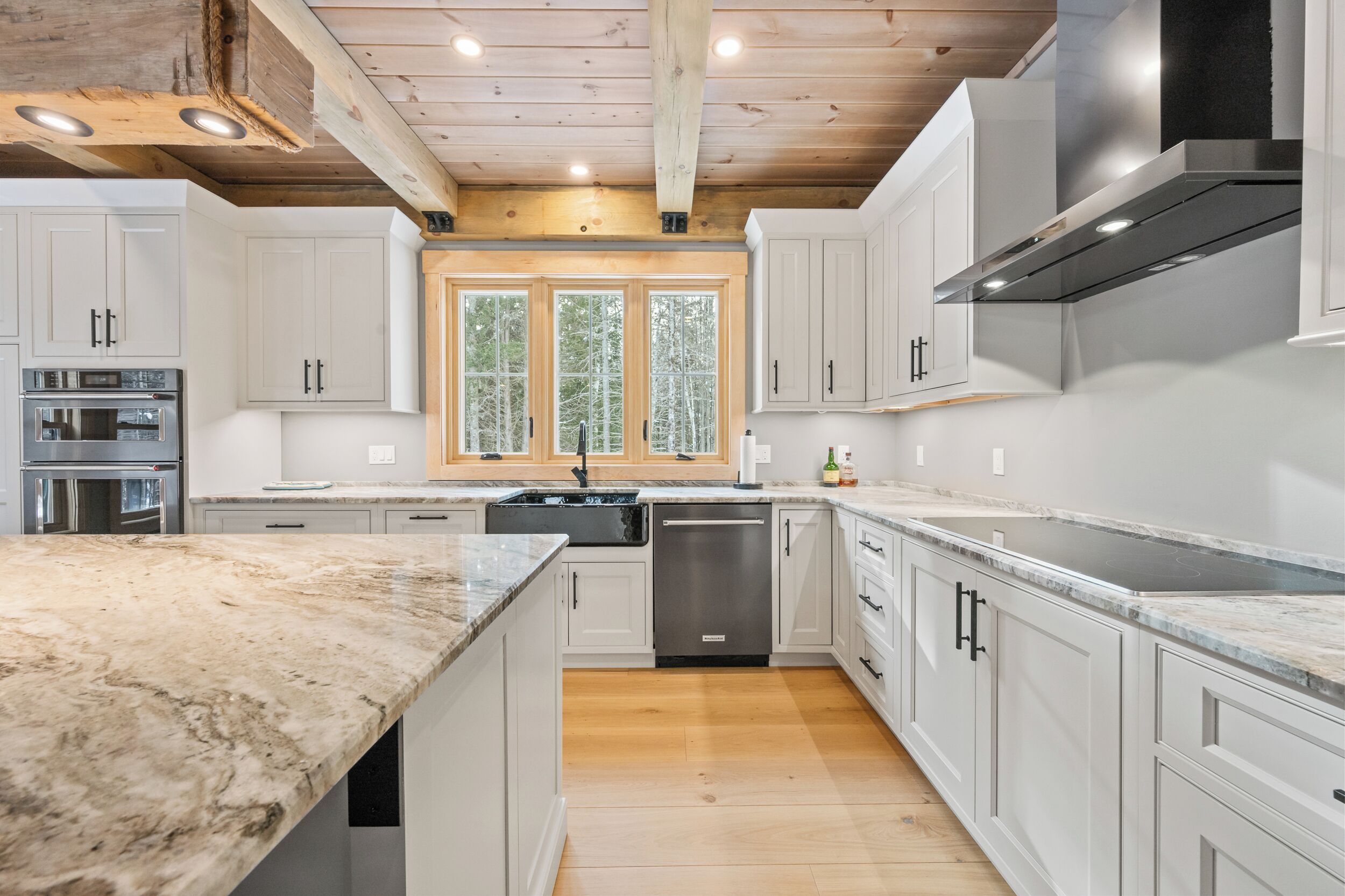 A modern kitchen with white cabinetry, a stainless steel dishwasher, and a large window.