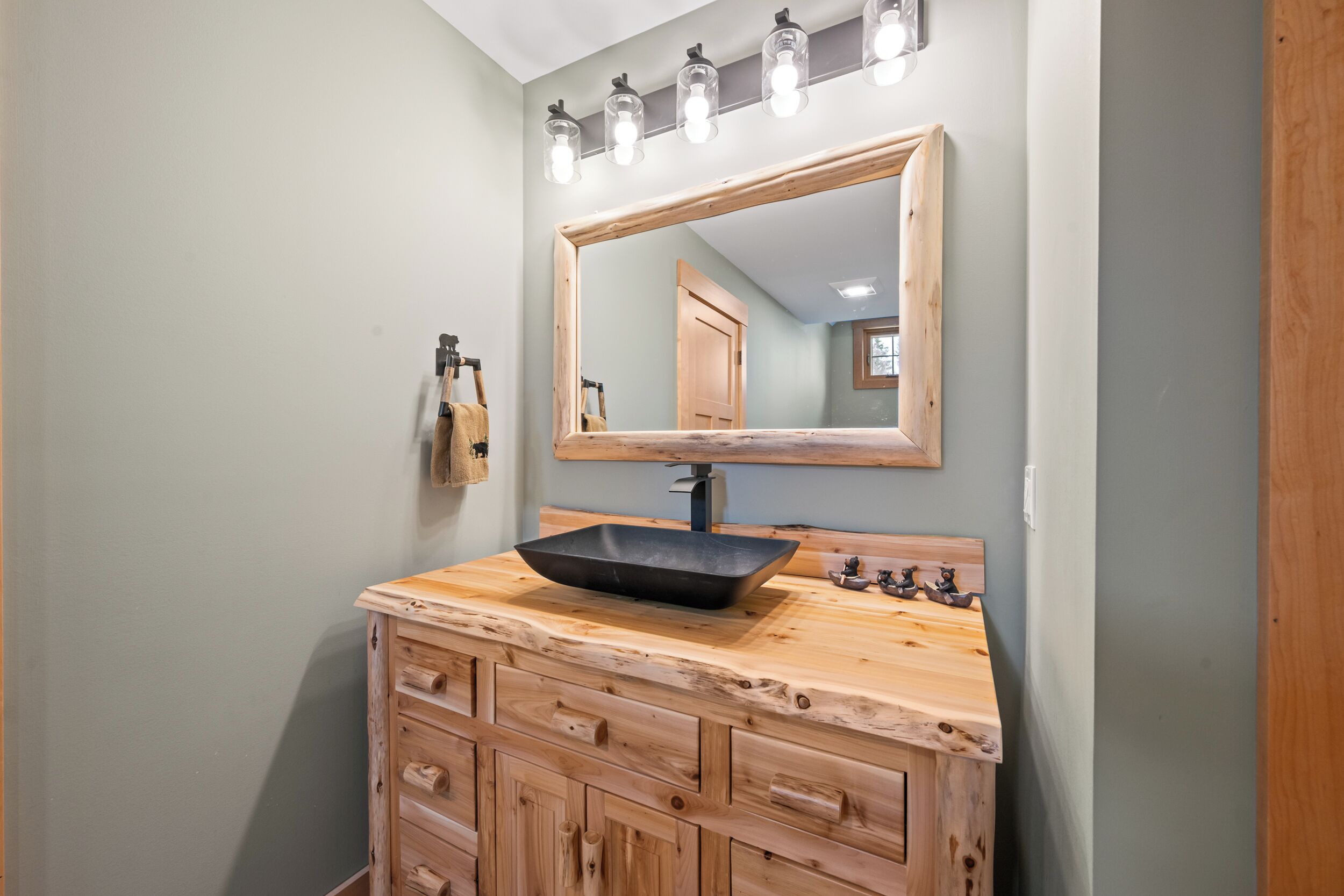Une salle de bain avec un meuble-lavabo en bois, un lavabo noir et un miroir avec des lumières au-dessus.