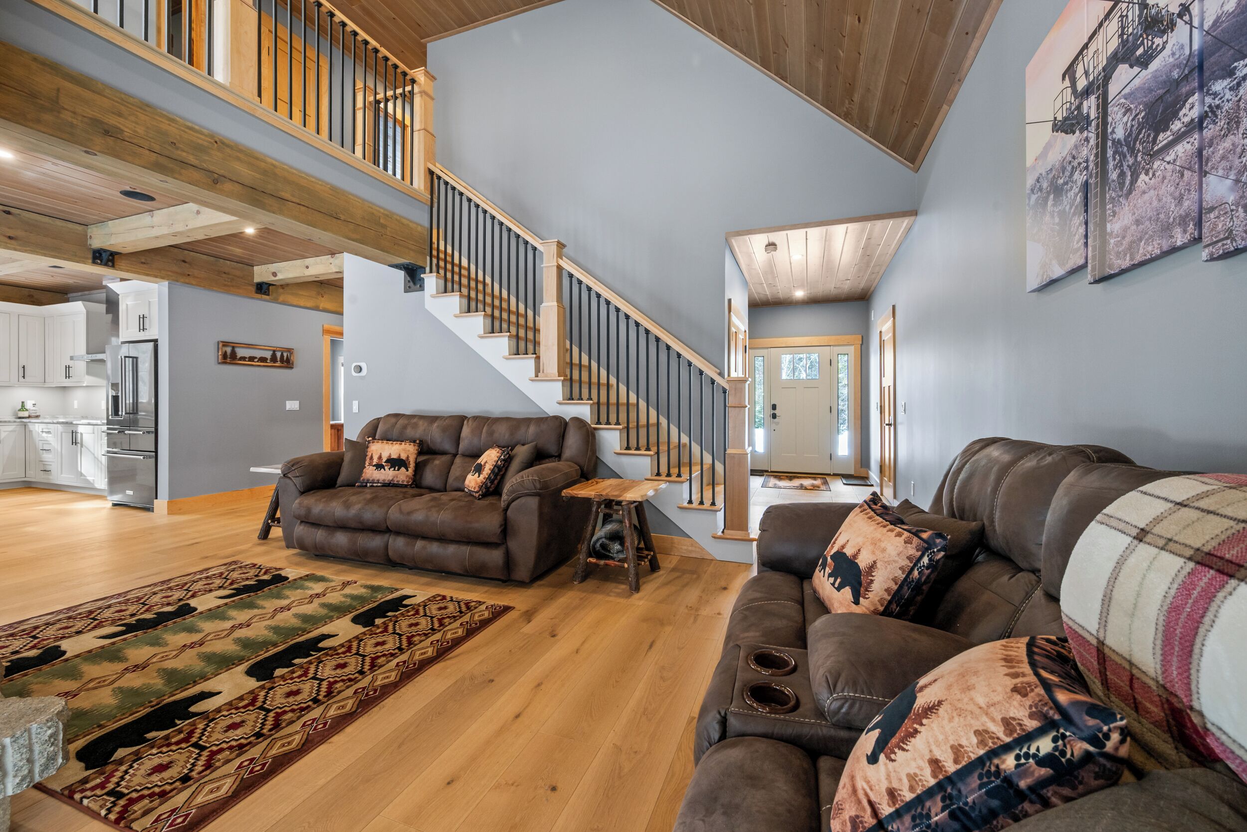 A spacious living room with a high ceiling, wooden staircase, and a kitchen in the background.