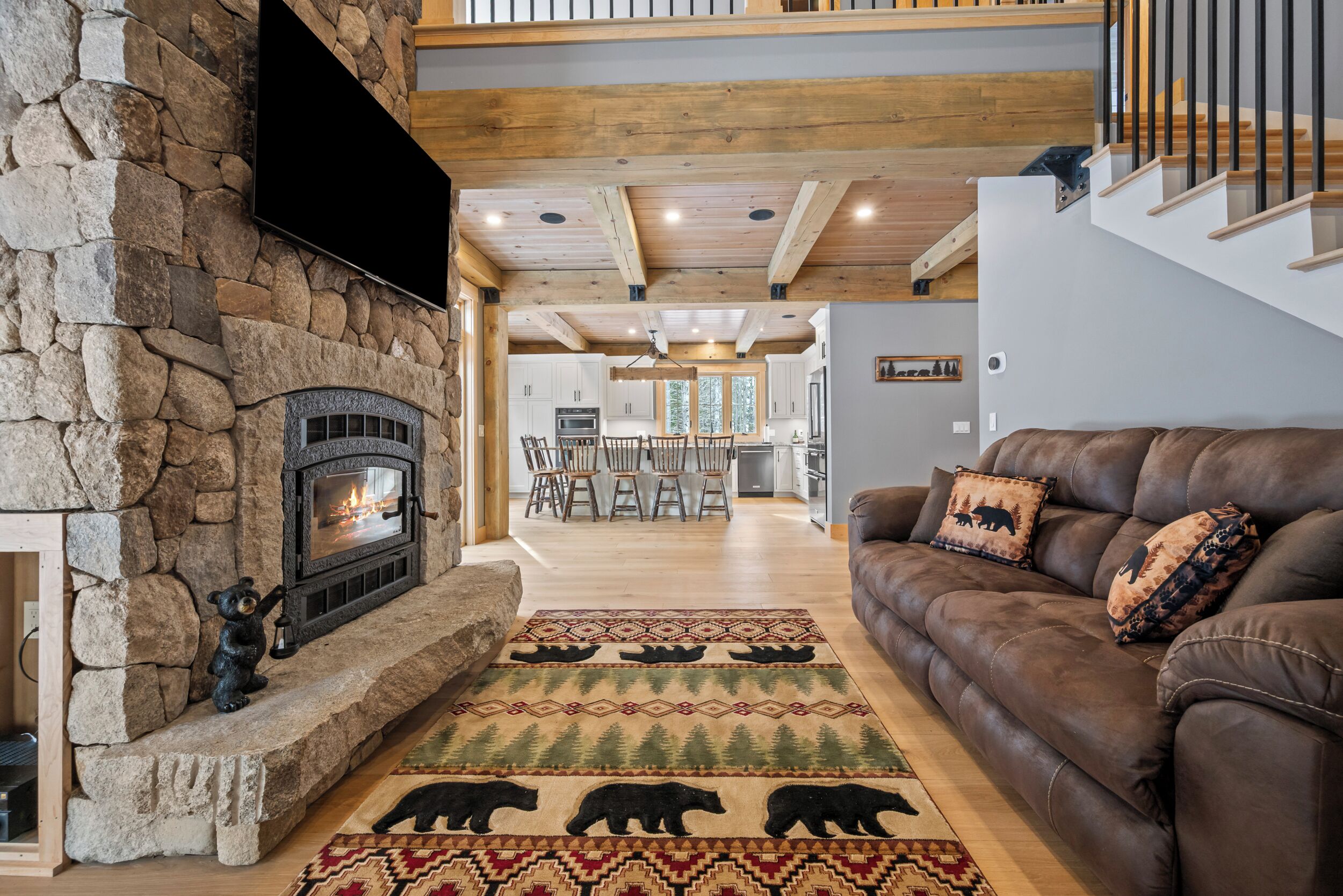 A stone fireplace with a bear figurine, a brown leather sofa with patterned cushions, and a dining area with wooden chairs.