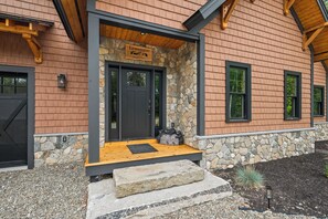 Ein Haus mit steinernem Fundament, einer Holzveranda und einem Schild mit Namen und Ort.
