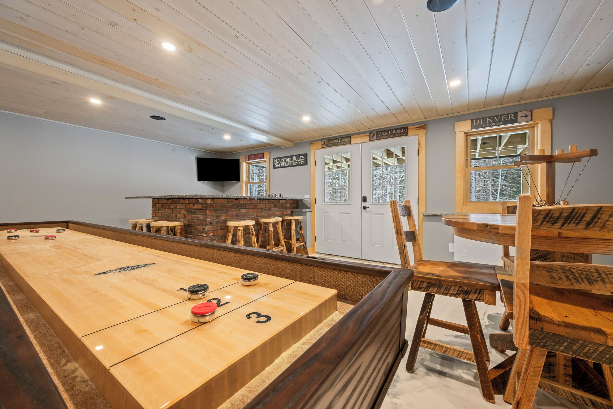 A room with a shuffleboard table, wooden chairs, a bar area, and a sign indicating the location as Aspen, Colorado.