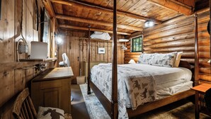 A wooden cabin bedroom with a bed, a dresser, a mirror, and a hanging light fixture. - The Boston | Waterfront on Mooselookmegtunic Lake | Pet Friendly (Rangeley)