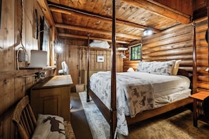 A wooden cabin bedroom with a bed, a dresser, a mirror, and a hanging light fixture. - The Boston | Waterfront on Mooselookmegtunic Lake | Pet Friendly (Rangeley)