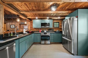A modern kitchen with wooden ceiling beams, teal cabinets, stainless steel appliances, and a sign indicating WiFi availability.