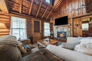 A cozy log cabin interior with a fireplace, wooden walls, and a television mounted above it.