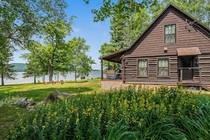 A cabin with a deck overlooking a lake, surrounded by greenery and trees.