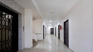 Un pasillo largo y estrecho con una pared de azulejos en un lado, una escalera con barandilla y puertas en el otro.