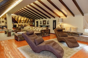A spacious living area with a high ceiling, wooden beams, and a fireplace.