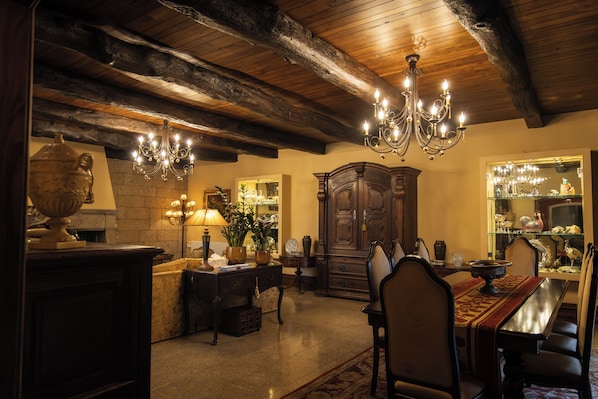 A dining area with a wooden ceiling, chandeliers, a large wooden cabinet, and a glass display case.