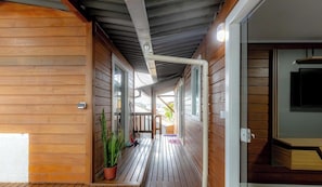A wooden exterior corridor with a covered porch, a potted plant, and a door leading to a room.