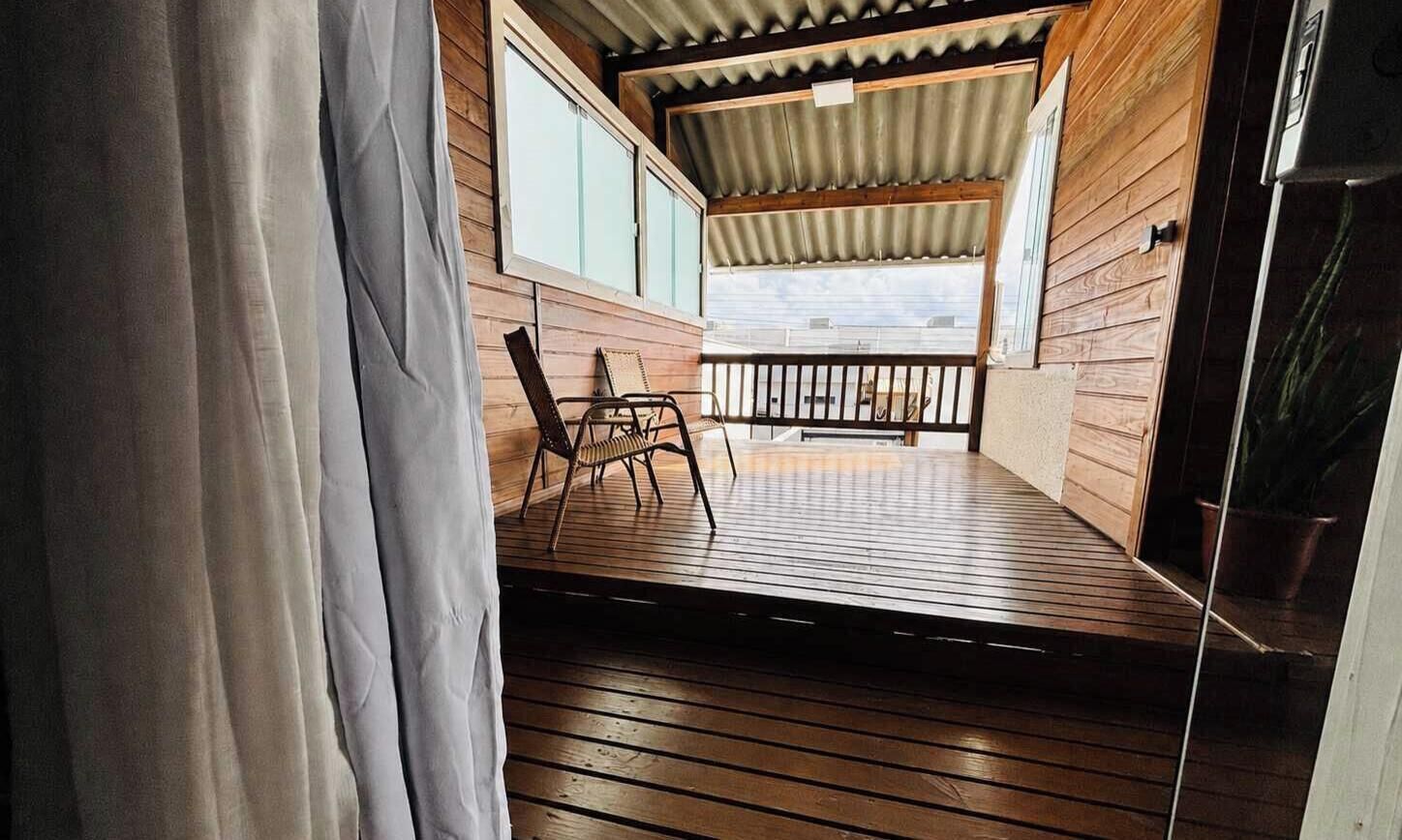 A wooden deck with a railing, a chair, and a view of the outside.