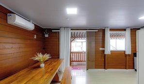 A room with wooden walls, a wooden bench, a potted plant, a white air conditioner, and a door leading outside.