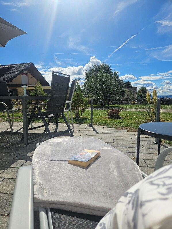 An outdoor seating area with a table and chairs, a book on the table, and a view of the sky and buildings in the background.