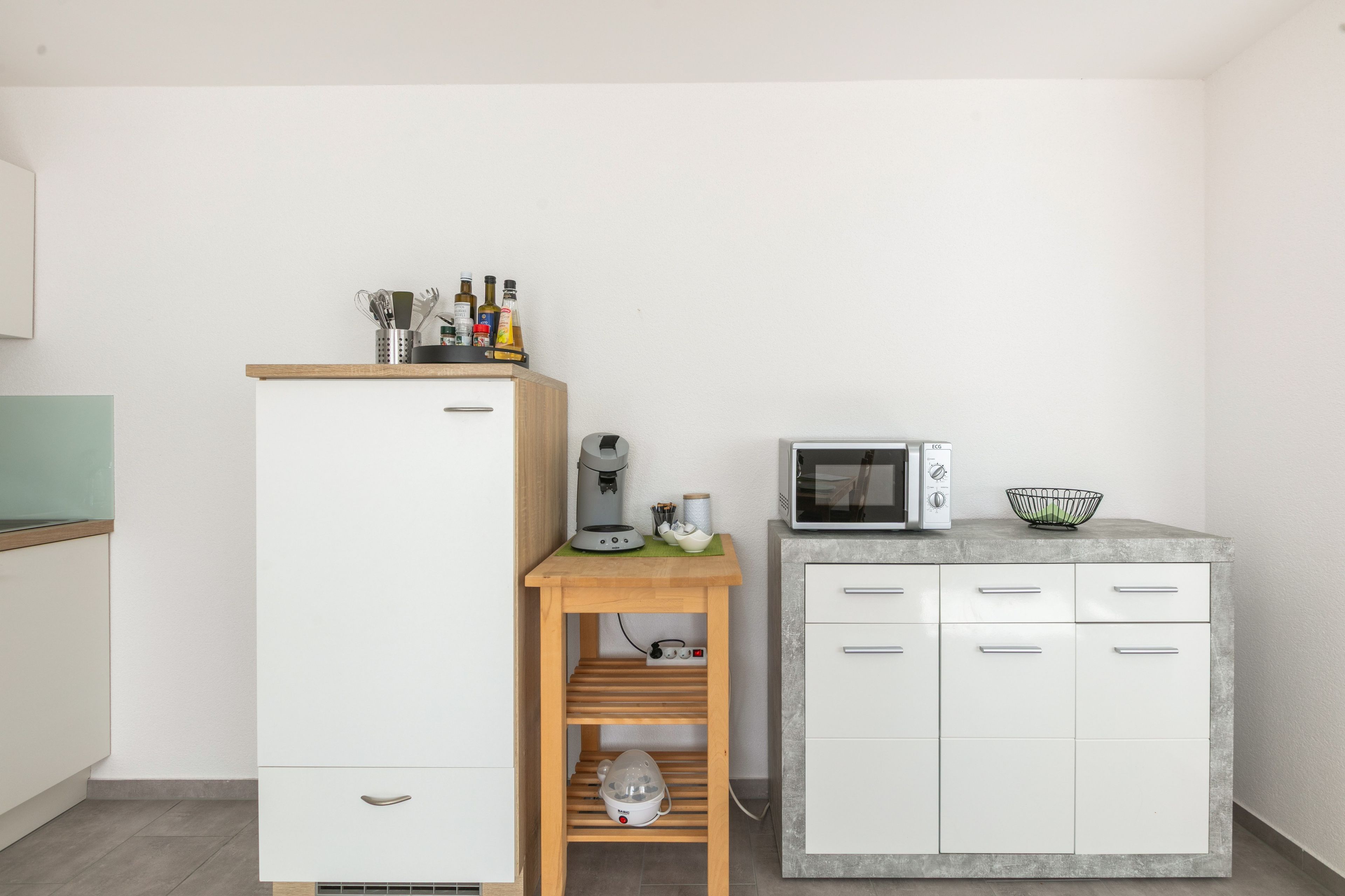Une petite cuisine équipée avec un réfrigérateur blanc, un four à micro-ondes et une petite table en bois, ainsi qu’une bouilloire et des tasses.