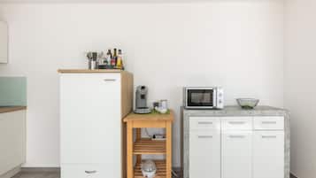 Une petite cuisine équipée avec un réfrigérateur blanc, un four à micro-ondes et une petite table en bois, ainsi qu’une bouilloire et des tasses.