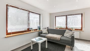 A modern living room with a grey sofa, white coffee table, and a window with a curtain.