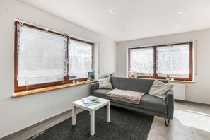 A modern living room with a grey sofa, white coffee table, and a window with a curtain.