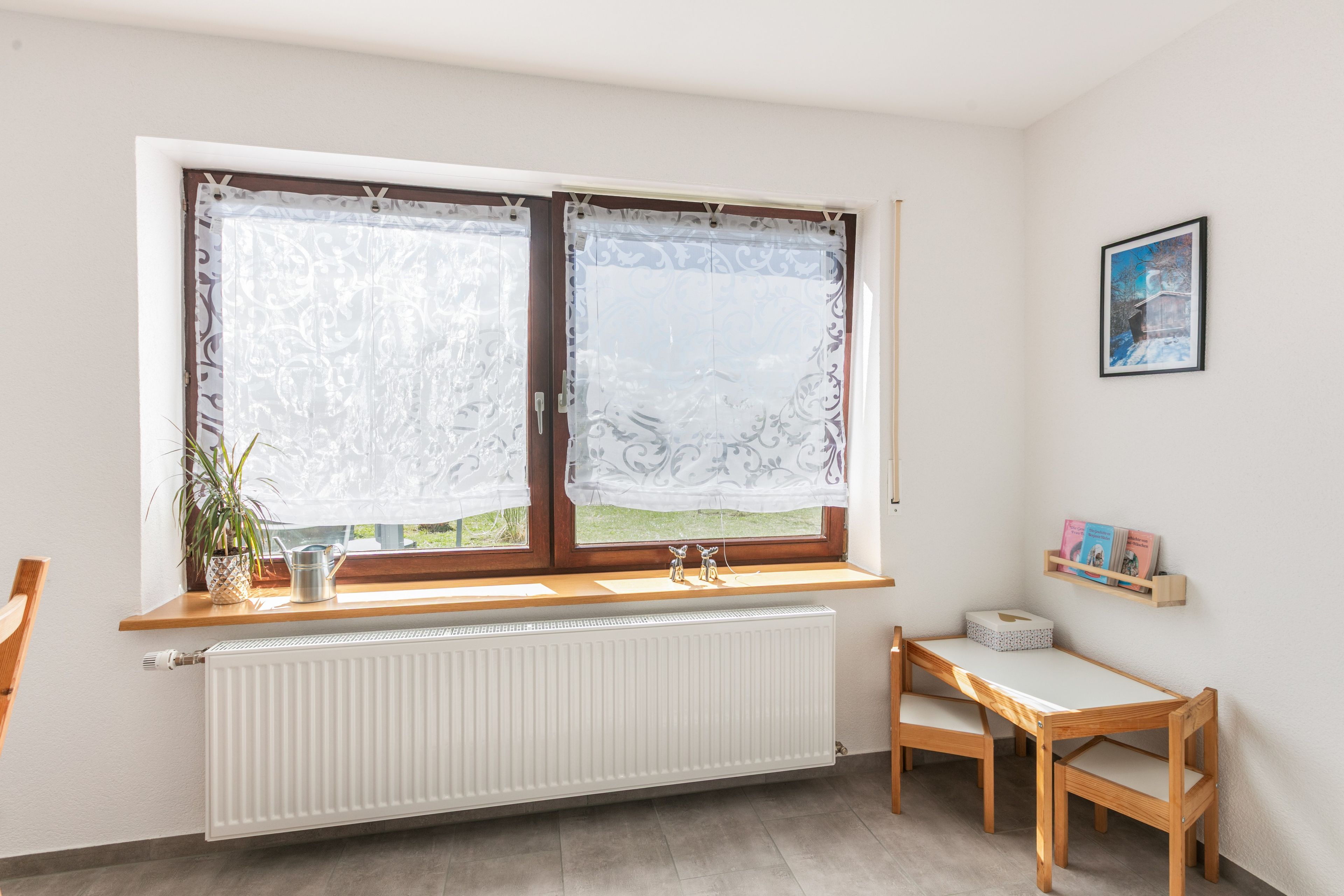 Une pièce avec une fenêtre, un radiateur, une chaise en bois et une étagère remplie de livres.