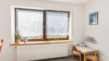 Une pièce avec une fenêtre, un radiateur, une chaise en bois et une étagère remplie de livres.