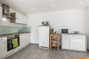 A modern kitchen with white cabinets, a built-in oven, a microwave, and a coffee machine.