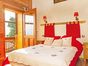 Ein Schlafzimmer mit Holzbalkendecke, einem großen Fenster, einem Bett mit rot-weißer Bettwäsche und zwei Wandleuchten.