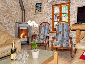 A cozy living room with a stone wall, a fireplace, two floral-patterned chairs, a sofa, and a table with glasses and a bottle.