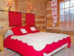 A wooden room with a bed, two wall-mounted lamps, and a window with a floral curtain.