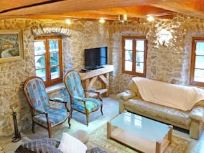 A stone-walled room with a television, two armchairs, a sofa, and a coffee table.